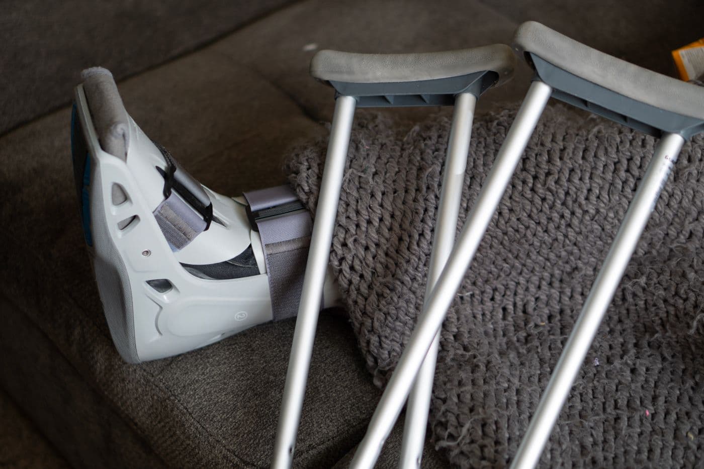 Orthopedic walking boot and crutches beside a sofa
